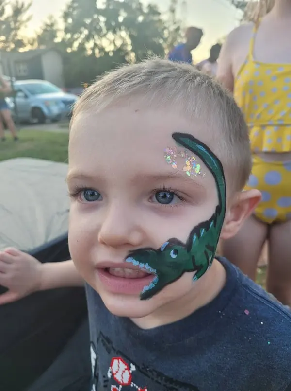 Child with a green dinosaur painted along his cheek