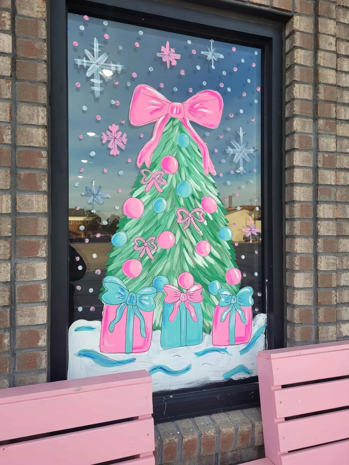 Window painted with a pastel pink Christmas tree and presents