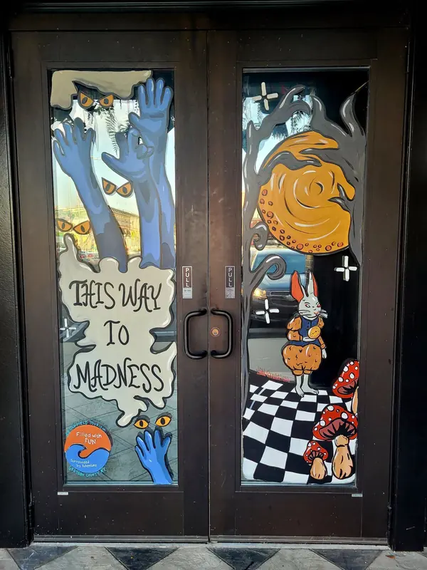 Theatre doors painted with This Way to Madness and reaching hands